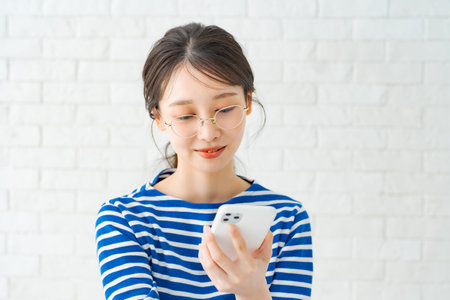 Smiling woman with glasses holding a smartphoneの写真素材