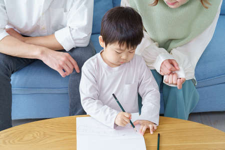 A boy working on drawing with a pencil and his parents watching over itの写真素材