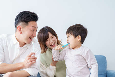 Parents and child brushing teeth on the sofaの写真素材