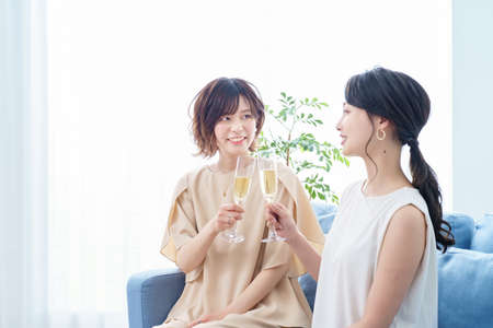 Two women chatting with champagne glasses in their hands with a smileの写真素材