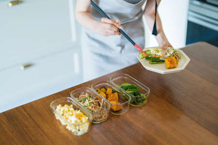 A woman who puts prepared side dishes on a plate on the tableの写真素材