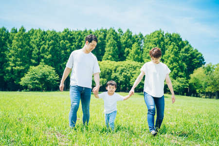 Parents and their child holding hands and walking on a sunny green spaceの写真素材