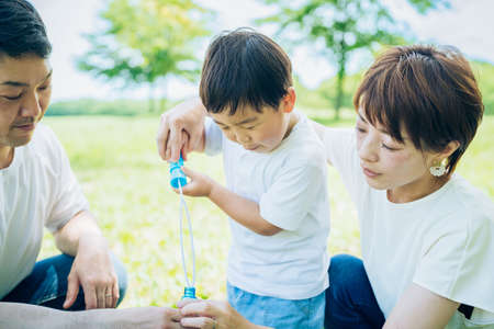 Parents and their child playing with soap bubbles at the parkの写真素材