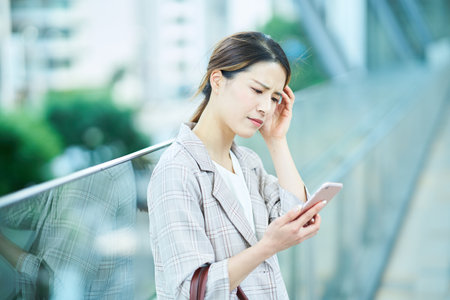 A young woman looking at a smartphone screen with a troubled expressionの販売画像