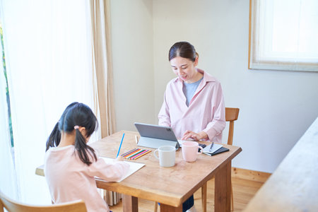 Girl drawing with her mother working at the table at homeの写真素材