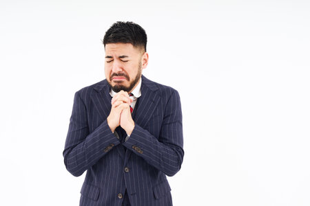 A man in a suit doing a praying pose and white backgroundの写真素材