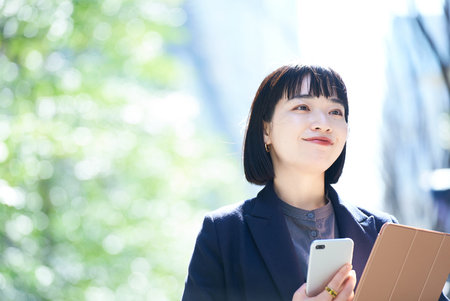 A woman holding a smartphone outdoorsの写真素材