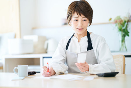 A woman in an apron checking receipts in the roomの写真素材