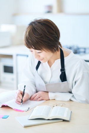 A woman in an apron studying by text at kitchenの写真素材