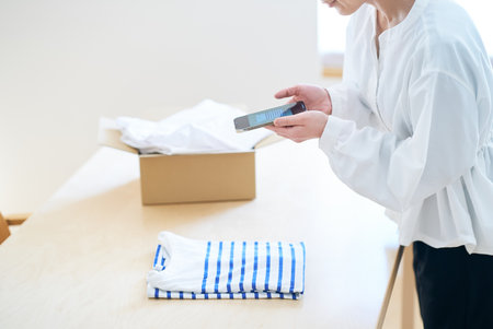 Woman photographing clothes with smartphone in the roomの写真素材