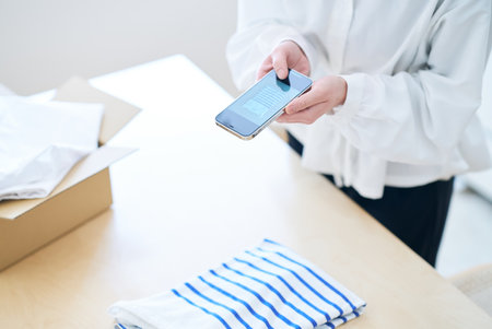 Woman photographing clothes with smartphone in the roomの写真素材