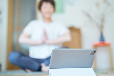 A woman stretching in a room while looking at a tablet PC screenの写真素材