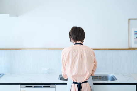 Rear view of a woman washing dishes in the kitchenの写真素材