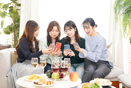 Four women talking while looking at their smartphones indoorsの写真素材