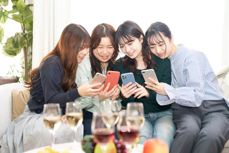 Four women talking while looking at their smartphones indoorsの写真素材