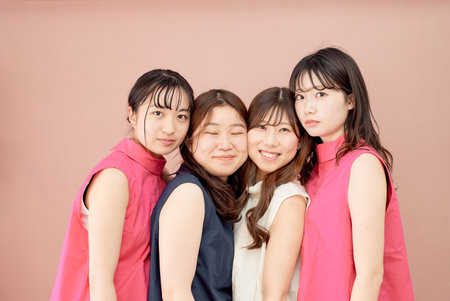 A group of four young women standing in front of a color background