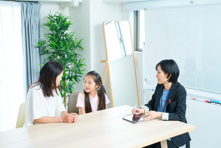 Conversation scene of a woman in a suit with a parent and child in the roomの写真素材