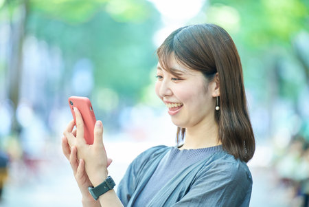 Young woman looking at smartphone screen on fine dayの写真素材