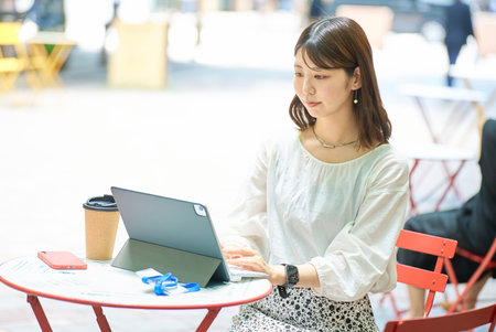 A woman operating a PC outdoors on fine dayの写真素材