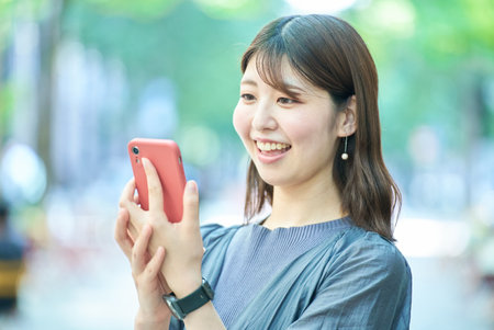 Young woman looking at smartphone screen on fine dayの写真素材