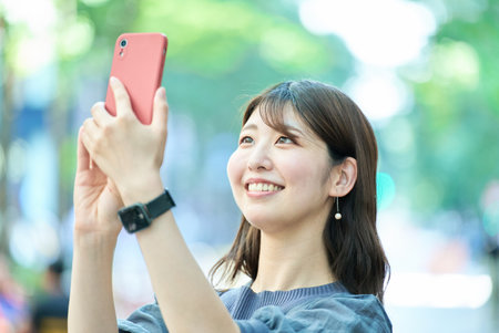 young woman holding a smartphone outdoorsの写真素材