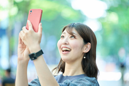 young woman holding a smartphone outdoorsの写真素材