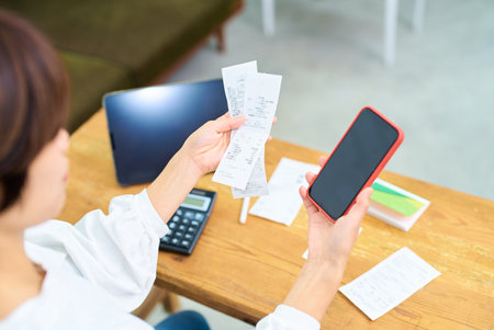 A woman holding a receipt and smartphone indoorsの写真素材