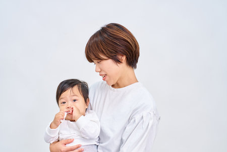 young woman holding an infant and white backgroundの写真素材