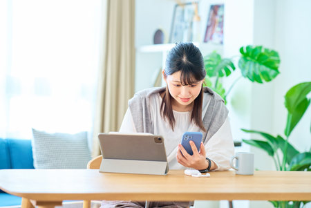 Young woman looking at smartphone and tablet PC screen in the roomの写真素材