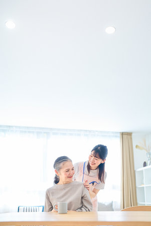 Young woman in apron and senior woman having a conversation at homeの写真素材