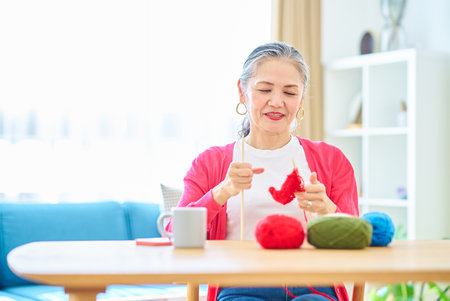 Senior woman enjoying knitting yarn in the roomの写真素材