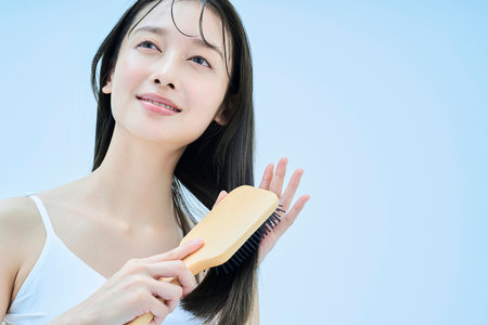 long-haired woman brushing her hair with smileの写真素材
