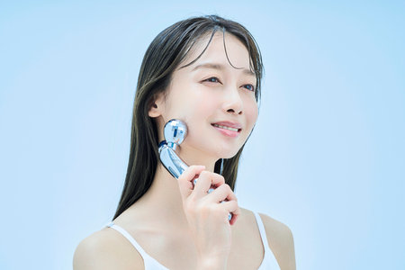 Young woman self-massaging her face and pale blue background