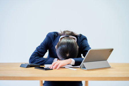 A woman in a suit working at a desk looking tiredの写真素材