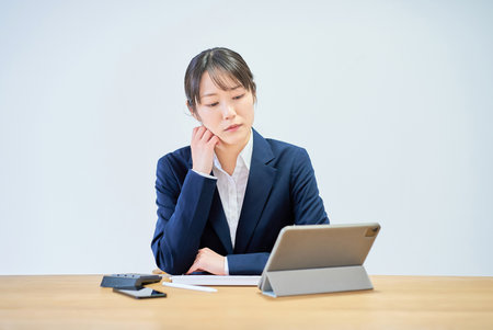 A woman in a suit working at a desk looking tiredの写真素材