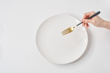 A white plate on the white table and woman's hand holding a  forkの写真素材