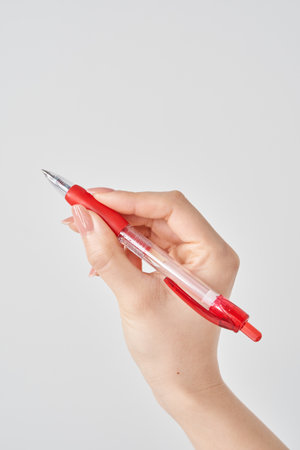 White background with female hand holding red ballpoint penの写真素材