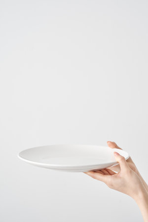 Woman's hand holding an empty plate and white backgroundの写真素材