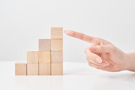 Wooden building blocks stacked in a staircase shape and a woman's hand pointingの写真素材