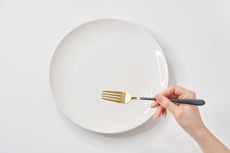 A white plate on the white table and woman's hand holding a  forkの写真素材