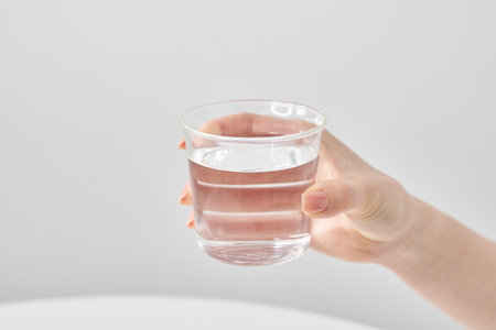 Woman's hand holding a glass of water and white backgroundの写真素材
