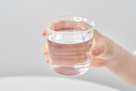 Woman's hand holding a glass of water and white backgroundの写真素材
