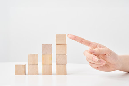 Wooden building blocks stacked in a staircase shape and a woman's hand pointingの写真素材