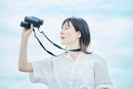 Young woman looking at distant view through binocularsの写真素材