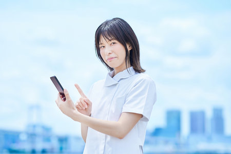 A young woman wearing a white coat operating a smartphone outdoorsの写真素材