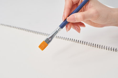 Woman's hand holding a paintbrush and white backgroundの写真素材
