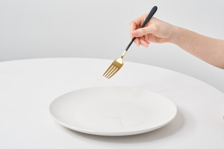 A white plate on the white table and woman's hand holding a  forkの写真素材