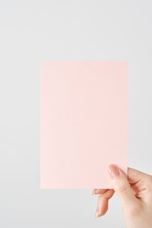 Woman's hand holding a pink piece of paper and white backgroundの写真素材