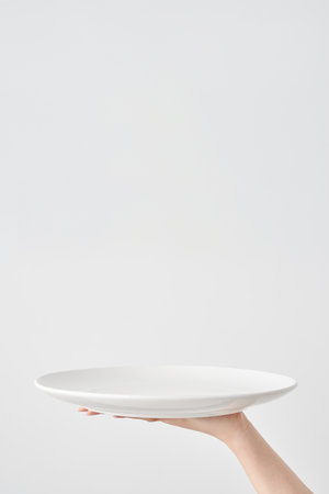 Woman's hand holding an empty plate and white backgroundの写真素材