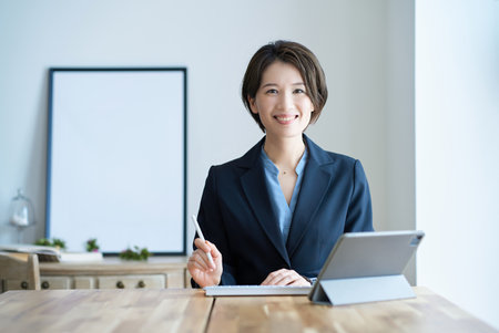 A woman in a suit sitting in front of a tablet PC indoorsの写真素材